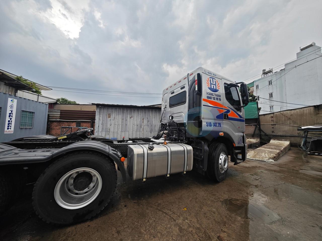 Xe đầu kéo màu bạc với khung chassis dài, bình nhiên liệu kim loại và cabin trang trí họa tiết cam xanh ngაა